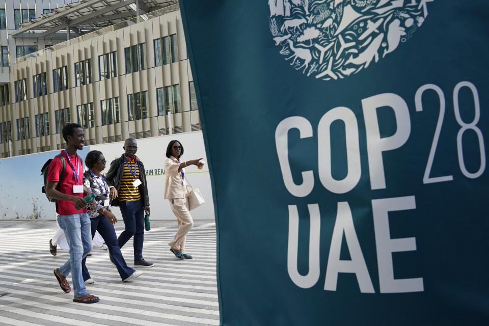 People walk near a logo for the COP28 U.N. Climate Summit, Wednesday, Nov. 29, 2023, in Dubai, United Arab Emirates. (AP Photo/Joshua A. Bickel)