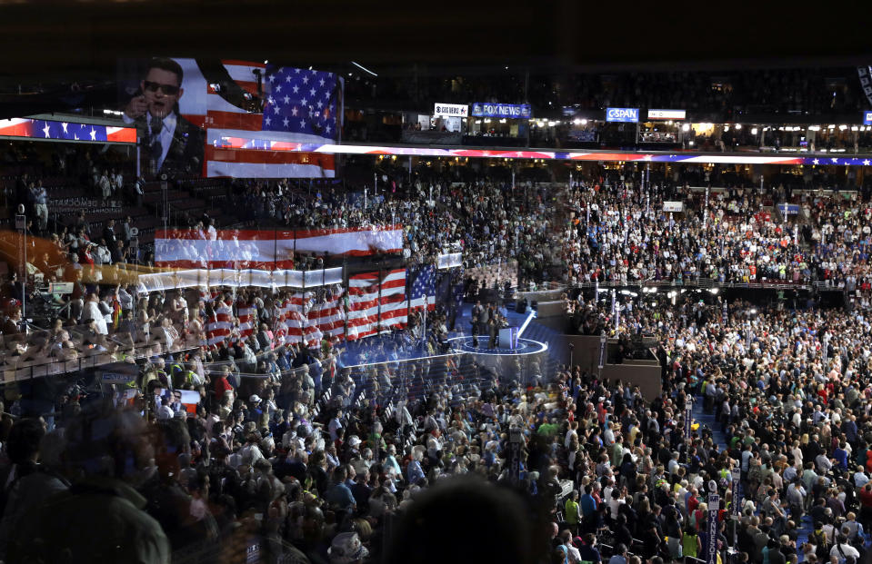 FILE - In this July 26, 2016, file photo the stage is reflected on a glass window on the suite level at Wells Fargo Arena as Timmy Kelly sings the national anthem before the start of the second day session of the Democratic National Convention in Philadelphia. The coronavirus pandemic is forcing Democrats and Republicans to take a close look at whether they'll be able to move forward as planned this summer with conventions that typically kick off the general election season. (AP Photo/John Locher, File)