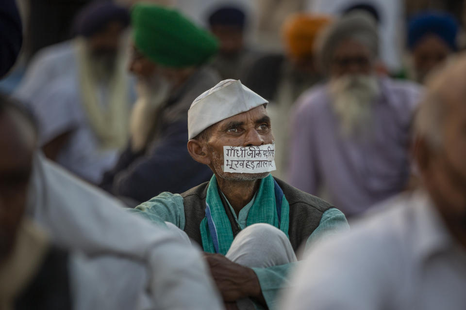 FILE - In this Wednesday, Dec. 9, 2020, file photo, a farmer sits with a tape across his mouth that reads, "Walking in the footsteps of Gandhi, I am on a hunger strike", as farmers protesting against new farm laws block a major highway at the Delhi-Uttar Pradesh state border, India. They are demanding the repeal of laws passed by Parliament in September that they say will favor large corporate farms, devastate the earnings of many farmers and leave those who hold small plots behind as big corporations win out. Modi has billed the laws as necessary to modernize Indian farming. (AP Photo/Altaf Qadri, File)