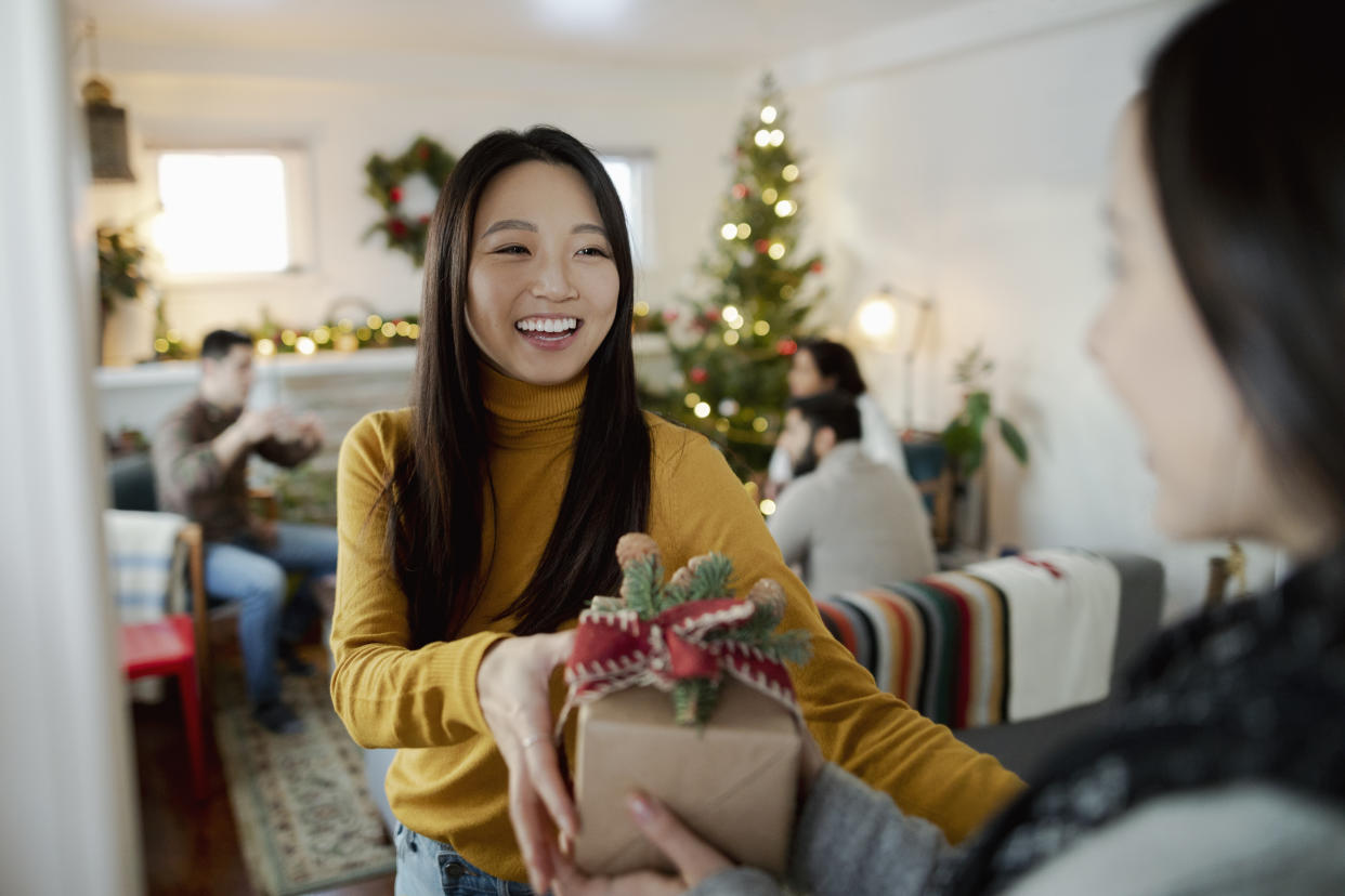 Happy young woman greeting friend with Christmas gift in doorway
