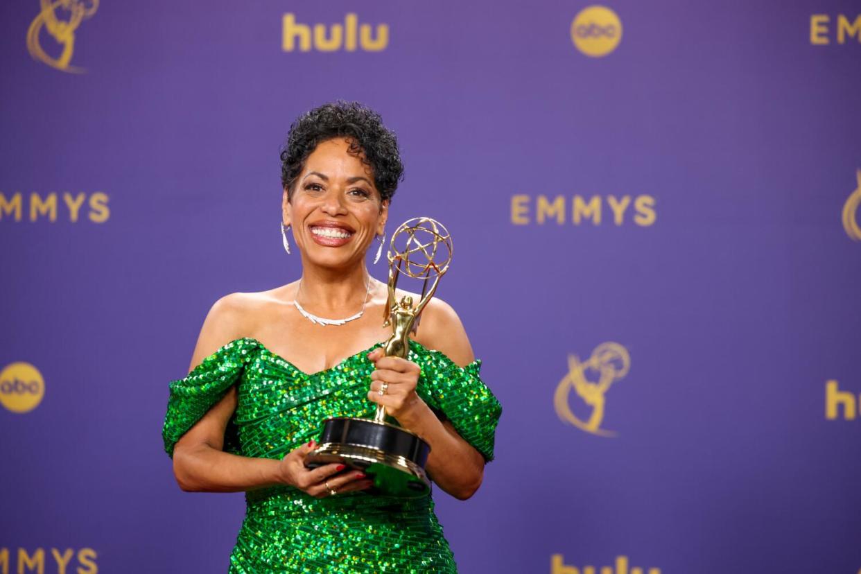 Liza Colon-Zayas, in a green dress, smiles and holds an Emmy