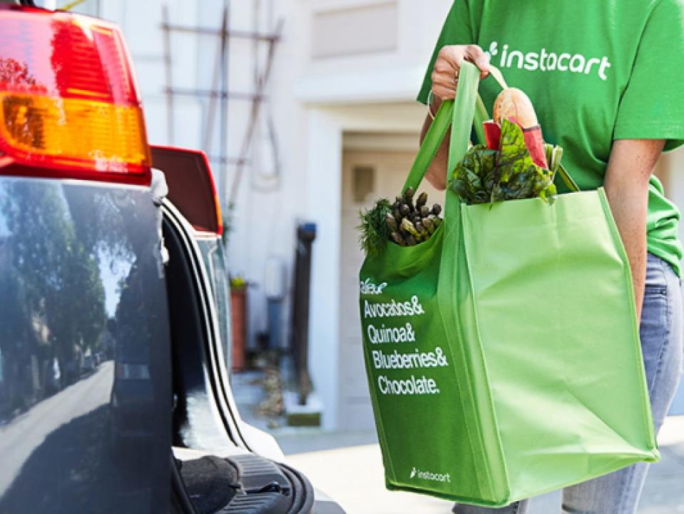 a person in a green shirt carrying a bag of groceries into a trunk for an online order