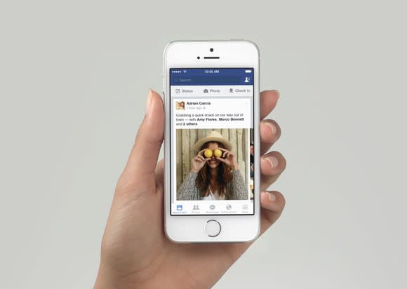 A hand holding a phone with the Facebook news feed loaded.