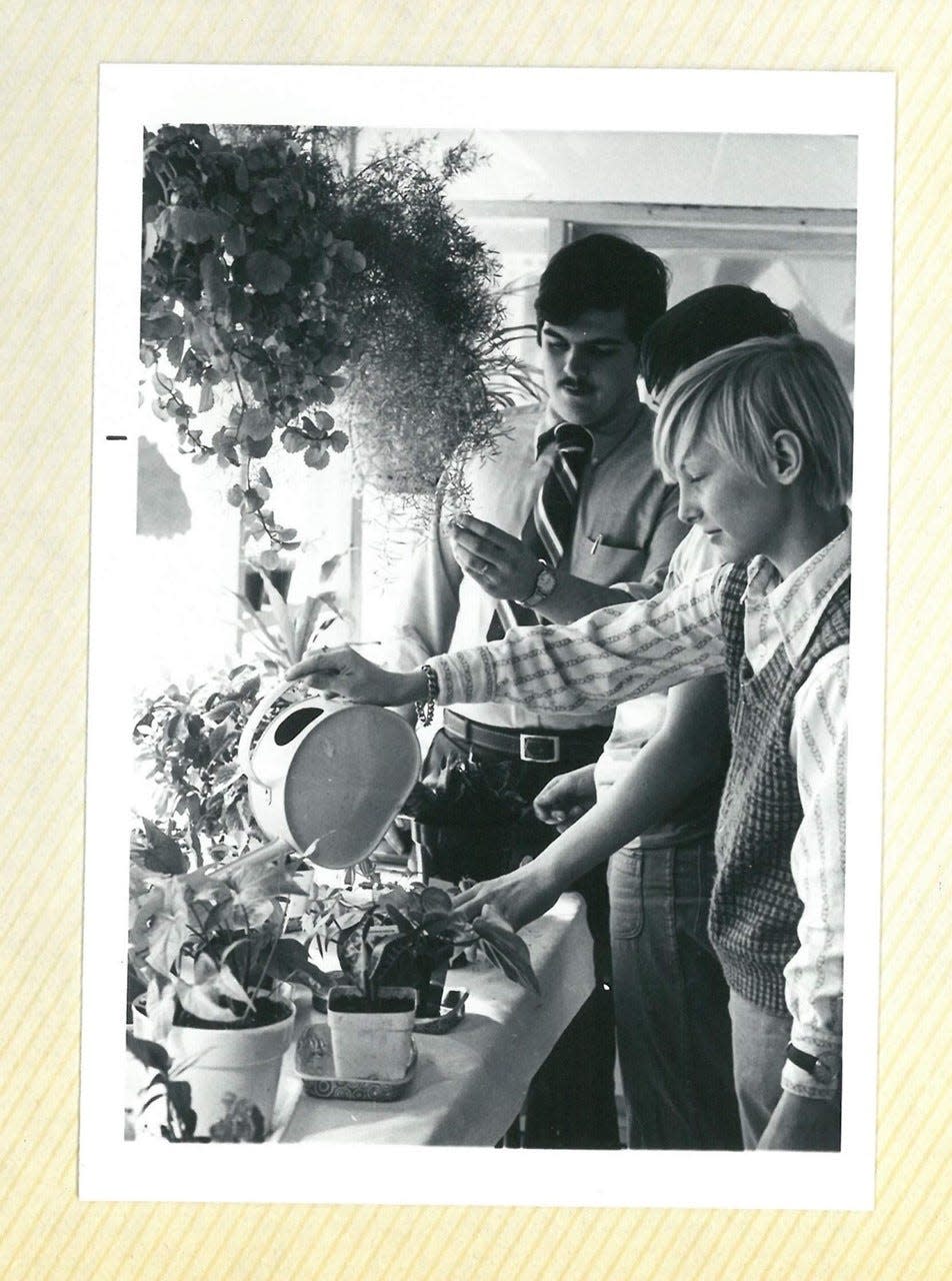 This photo shows Charlie Howard, at right in the foreground, and Bob Lister, in the background wearing a tie, at the Portsmouth High School greenhouse in the late 1970s.