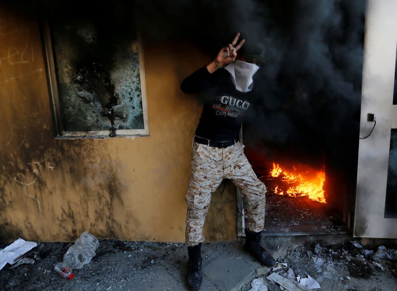 A member of Hashd al-Shaabi (paramilitary forces) flashes the victory sign as he stands next to a reception room of the U.S. Embassy with fire, during a protest to condemn air strikes on bases belonging to Hashd al-Shaabi (paramilitary forces), in Baghdad