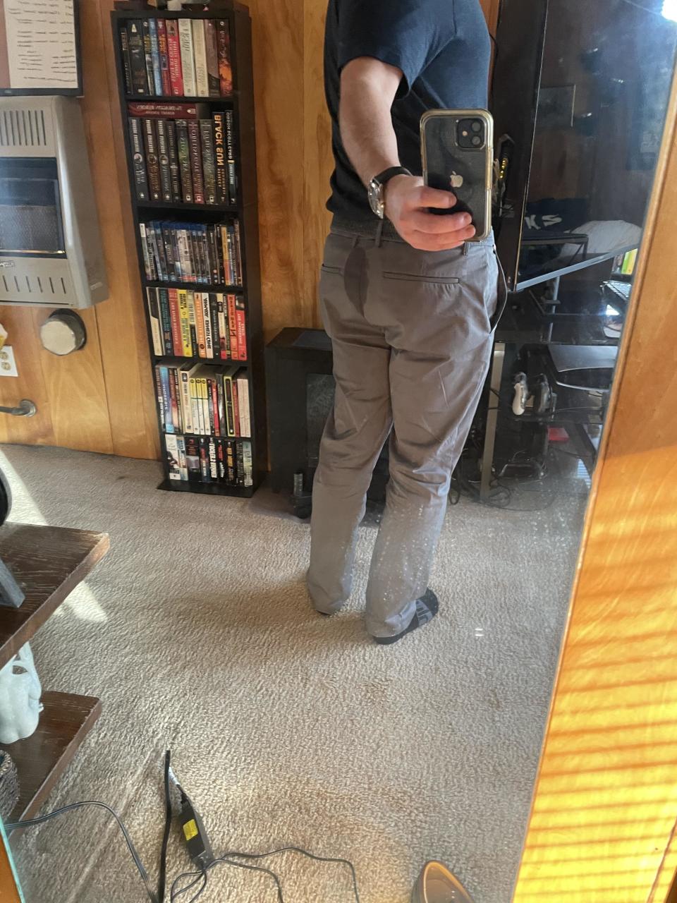 A person in a mirror selfie, with their face obscured by the phone, wearing business casual attire and pants with sweat on the butt