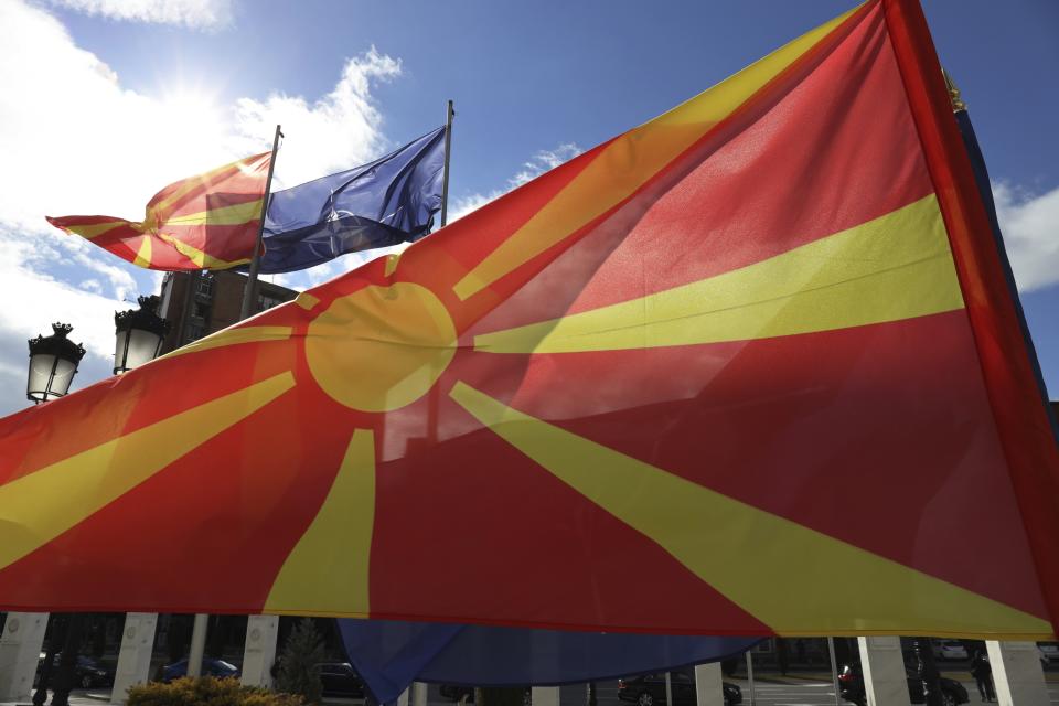 Macedonian and NATO flag wave in front of the government building during a ceremony in Skopje, Tuesday, Feb. 12, 2019. Macedonian authorities began removing official signs from government buildings to prepare for the country's new name: North Macedonia. (AP Photo/Dragan Perkovksi)