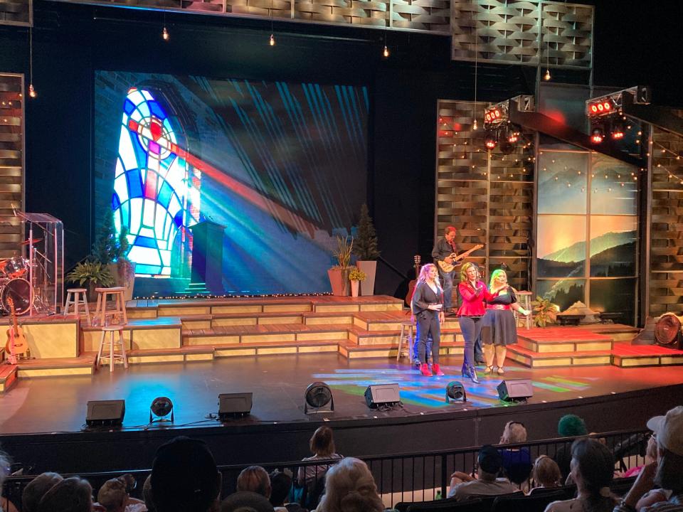 A concert at Dollywood with a stained glass cross on a screen in the background