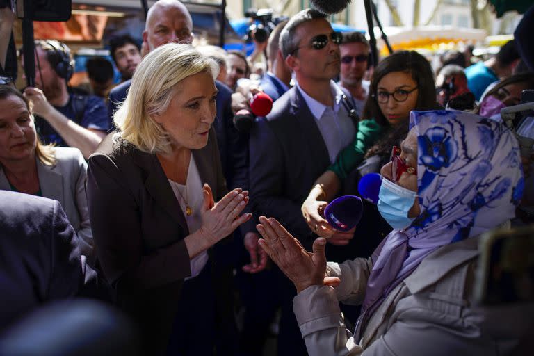 La candidata de extrema derecha Marine Le Pen habla con una mujer durante un acto de campaña en un mercado de Pertuis, Francia, el viernes 15 de abril de 2022. (AP Foto/Daniel Cole)