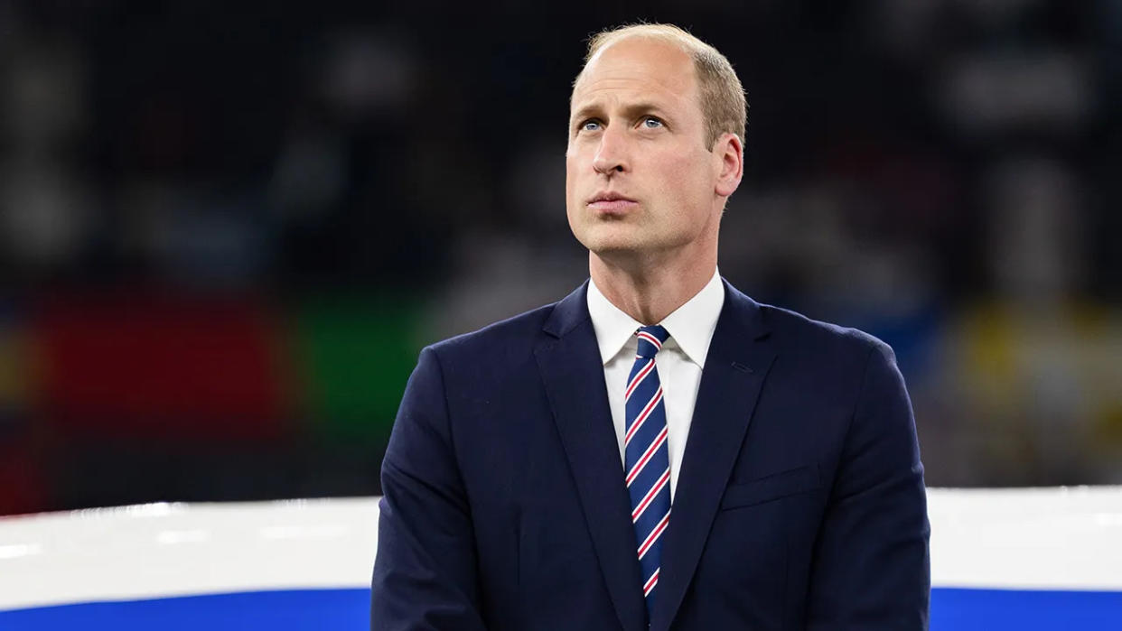 Prince William in a navy suit and striped tie looking up