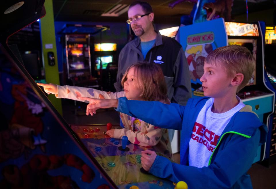 Seven-year-old Cecilia Wright, left, and her brother eight-year-old Dominic Wright, right, play the Teenage Mutant Ninja Turtles arcade as their father Kevin Wright gives them guidance on games he played as a kid at Secret Headquarters in Evansville, Ind., Friday, Nov. 25, 2022.