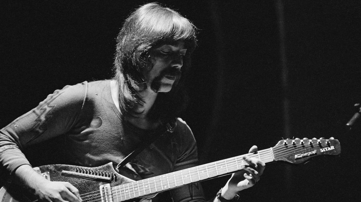  Steve Hackett of Genesis plays electric sitar on stage in a black and white portrait. 