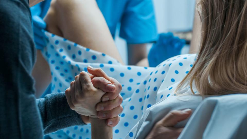 woman giving birth, husband holds her hand in support