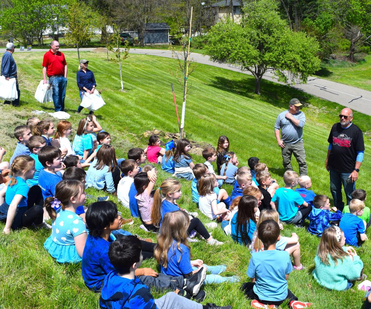 Kim Kellogg, right, and arborist Brent Schrock talked to Millersburg Elementary School first graders about the importance of trees by the newly planted red oak on the schoolgrounds. Tree City Committee members Rodney Arnold, back left, Brent Hofstetter and Beth Logan wait to pass out saplings to students.