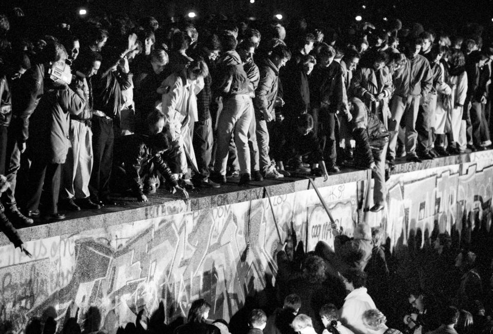 East and West German citizens celebrate as they climb the Berlin wall at the Brandenburg gate after the opening of the East German border was announced in Berlin, November 9, 1989.   REUTERS/Fabrizio Bensch (GERMANY ANNIVERSARY POLITICS)