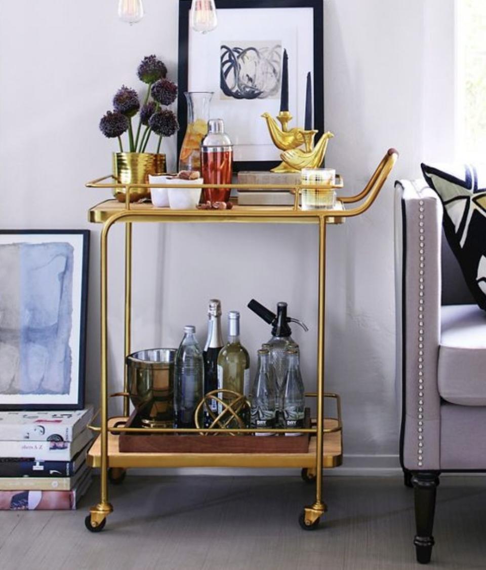 A golden bar cart with bottles on it