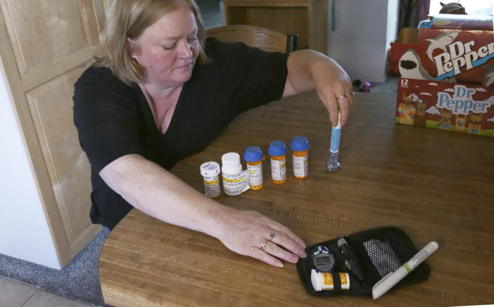 In this July 11, 2018, photo, Bridgett Snelten reaches for her prescriptions as she sits in her kitchen, in Sandy, Utah. (AP Photo/Rick Bowmer)