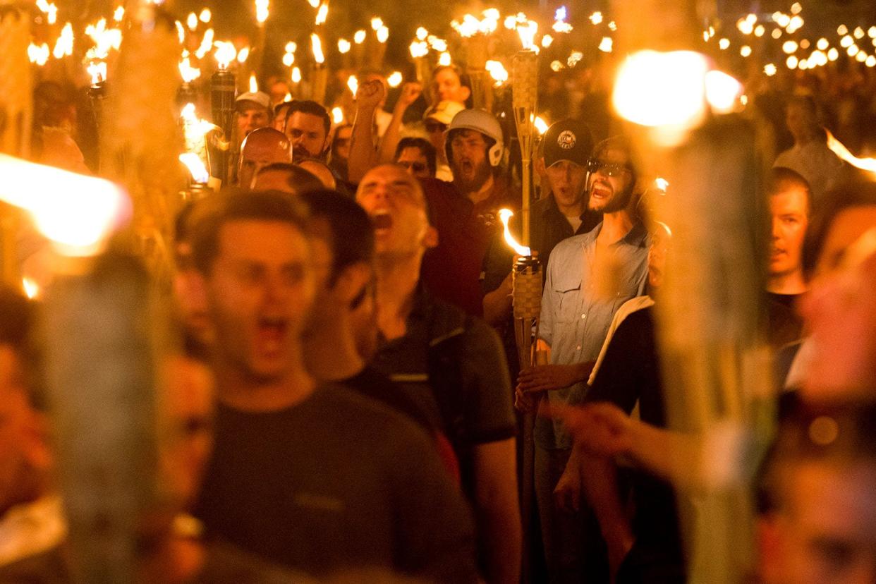 Participants in the Charlottesville Unite the Right rally are seen yelling, raising their fists, and holding tiki torches. 