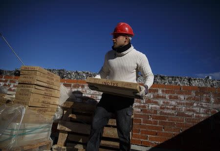 A worker carries tiles at a construction site of a residential block in the Valdebebas neighbourhood in Madrid December 10, 2014. REUTERS/Andrea Comas