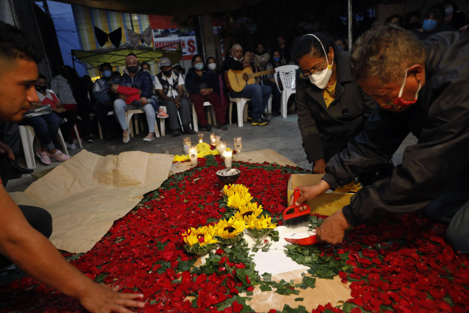 Family members carefully collect sunflowers, petals to be buried atop the grave of Luz Maria Gonzalez, during her cross raising ceremony in the family home in Valle de Chalco, on the outskirts of Mexico City, Friday, July 3, 2020. Gonzalez, 56, who had long suffered from asthma, diabetes, and hypertension, died two days after her 29-year-old son, who was hospitalized for breathing problems and a cough before dying of complications said to be related to pneumonia and undiagnosed diabetes. (AP Photo/Rebecca Blackwell)