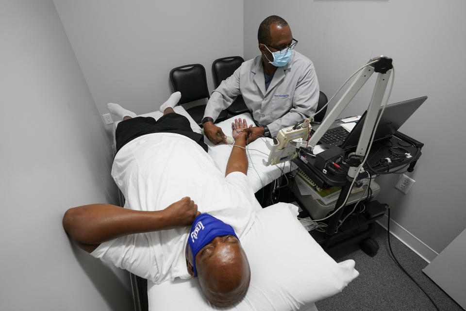 Larry Brown is tested by Dr. Jerry Smartt, Monday, Aug. 17, 2020, in Carmel, Ind. While hospitalized because of COVID-19 starting in March, doctors moved Brown to the ICU and started him on the ventilator while grappling with how to treat him. They tried the common antibiotic azithromycin, but his pneumonia grew worse. They administered the malaria treatment touted by President Donald Trump, hydroxychloroquine, but saw no progress. They put him in a medically induced coma, and attached him to an ECMO machine, which essentially did the job of his lungs by transferring oxygen into his blood. (AP Photo/Darron Cummings)