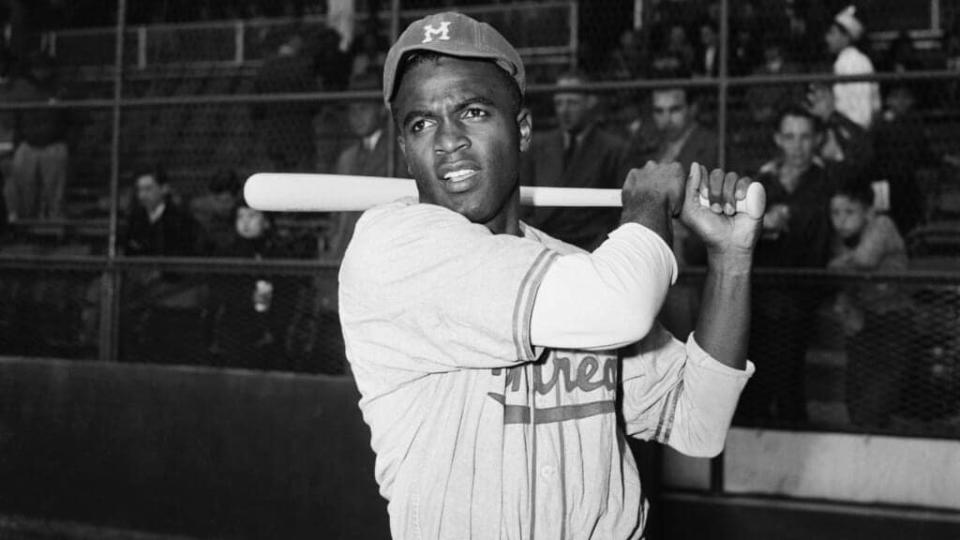 Jackie Robinson, the first Black man to be signed by a Major League baseball team, is shown in post-swing position in front of the stands. Robinson is wearing the uniform of then-Brooklyn Dodgers affiliate the Montreal Royals. (Getty Images)