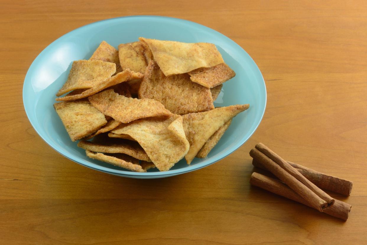 Cinnamon sugar pita bread chips in blue bowl with cinnamon sticks on wood background