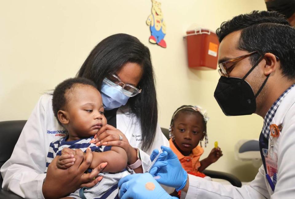 Dr. Nizar Dowla, right, gives a COVID-19 vaccine to 9-month-old Deji Adebayo while his mother, Dr. Emy Jean-Marie, and his sister, Emiola Adebayo, watch during a drive for children younger than 5 years old on Tuesday, June 28, 2022, at Borinquen Health Care Center in Miami.