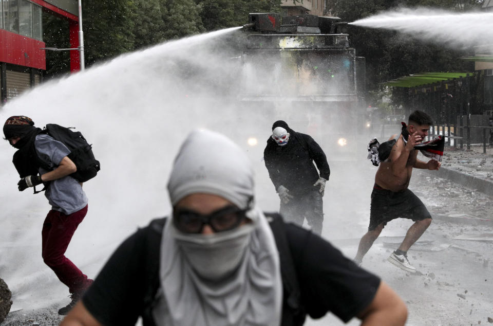 Anti-government protesters run from an advancing police water cannon in Santiago, Chile, Friday, Nov. 8, 2019. Chile's president on Thursday announced measures to increase security and toughen sanctions for vandalism following three weeks of protests that have left at least 20 dead. (AP Photo/Esteban Felix)