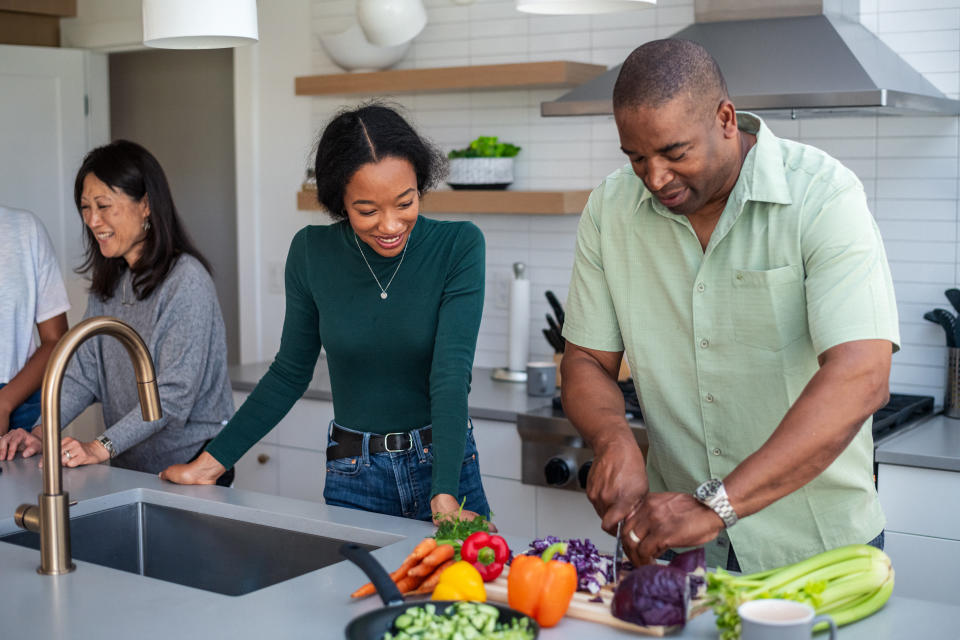 An Asian woman and her Black husband happily cook a fresh, vegetarian dinner with their mixed race teenage daughters, bonding at home.