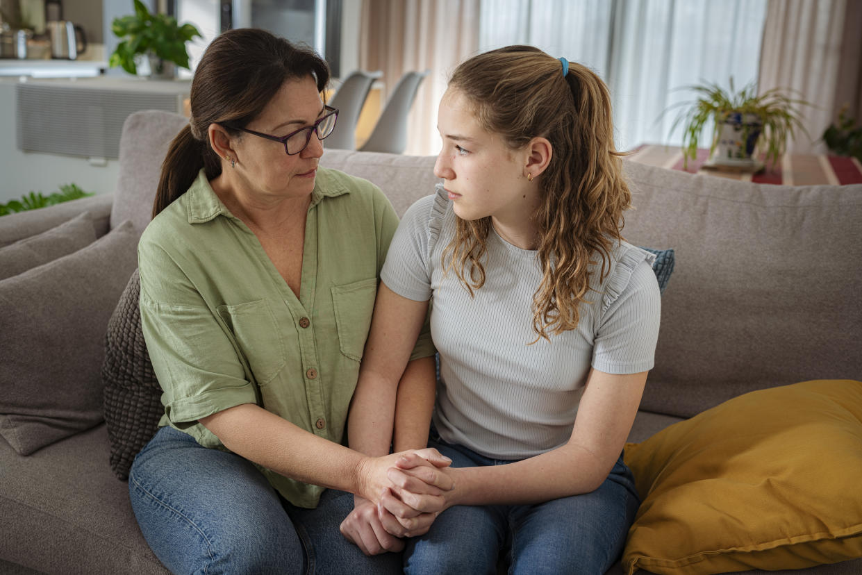 Mother and daughter sitting on sofa holding hands and talking about adolescence problems