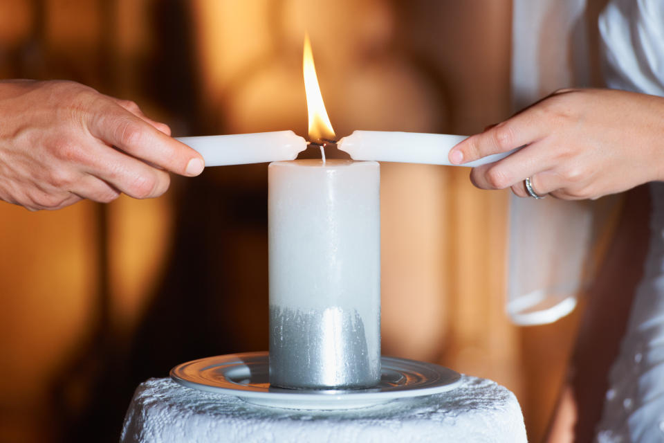 Two people light a unity candle together during a wedding ceremony, symbolizing the joining of two lives into one