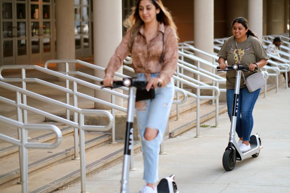 Two women ride Bird scooters in 2021 on the sidewalk outside of Prairie Surf Studio on Sheridan in downtown Oklahoma City.