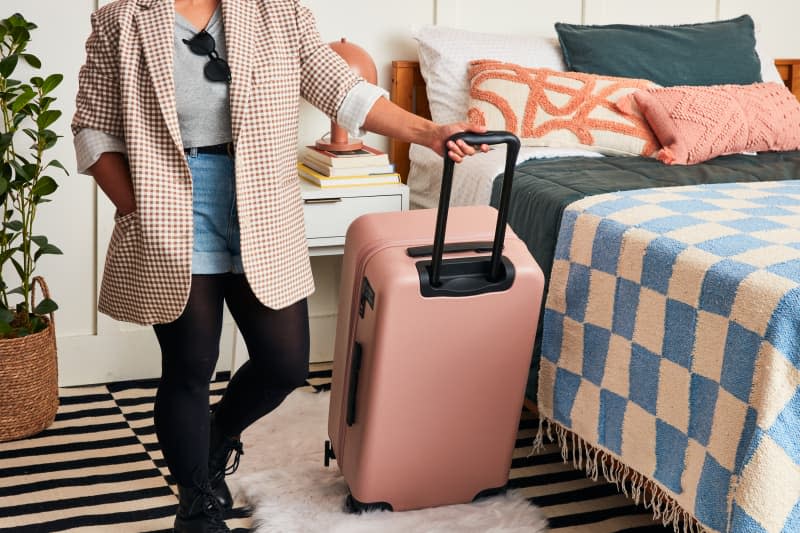 person holding a pink suitcase in a room getting ready to go