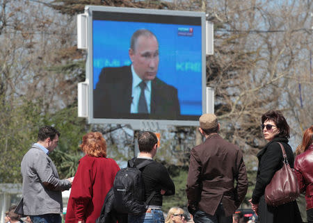 People stand next to an electronic screen showing nationwide call-in attended by Russian President Vladimir Putin on a street of the Black Sea port of Sevastopol, Crimea, April 16, 2015. Picture taken April 16, 2015. REUTERS/Pavel Rebrov