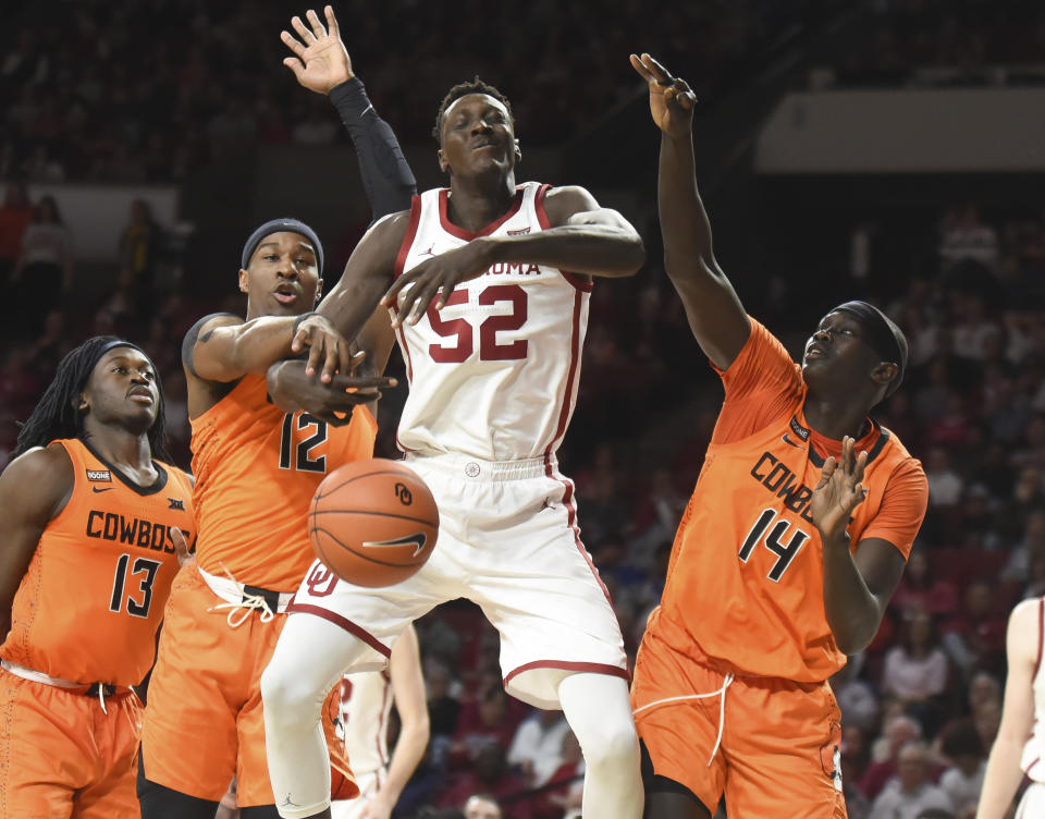 Oklahoma forward Kur Kuath (52) takes a foul as he goes up for a shot over Oklahoma St forward Cameron McGriff (12) and Yor Anei (14) during the second half of an NCAA college basketball game in Norman, Okla., Saturday, Feb. 1, 2020. (AP Photo/Kyle Phillips)