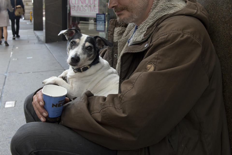 A homeless man holds his dog while begging in central London.