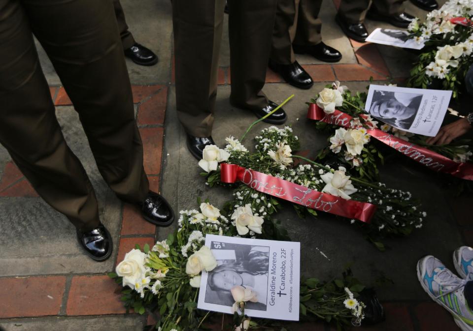 Flowers with images of slain students Geraldine Moreno, bottom, and Roberto Redman, top, lay at the feet Bolivarian National Guard officers outside their headquarters where a women's march arrived to protest repression against anti-government demonstrators in Caracas, Venezuela, Wednesday, Feb. 26, 2014. Moreno was near her home in Valencia watching students defend a barricade at the corner of her street when national guardsmen rushed in and fired rubber bullets at close range, hitting her in the face. She died from brain injuries on Saturday. Redman was shot and killed in a standoff with police on Feb. 12 in Caracas at the end of an opposition protest. (AP Photo/Fernando Llano)