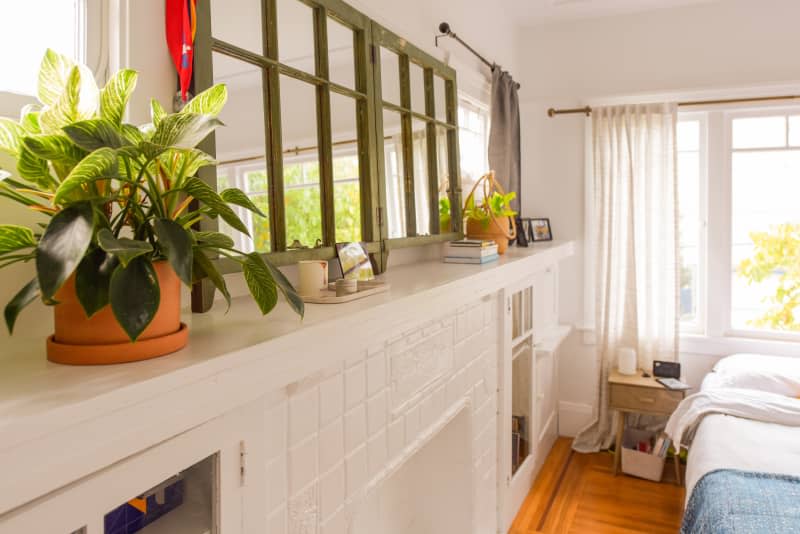 Potted plant and mirrors sit atop white fireplace unit.