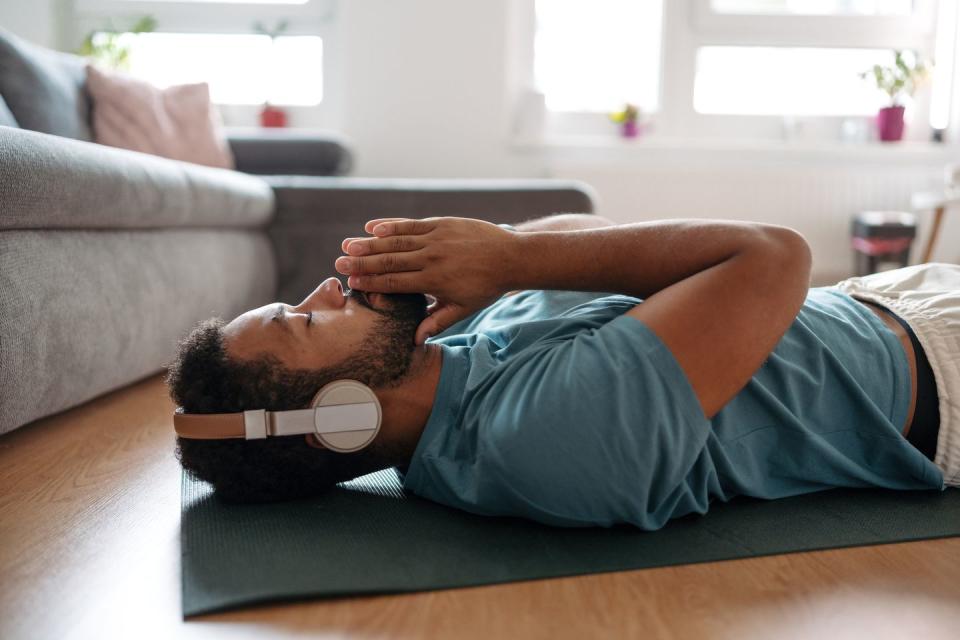 the single man meditating alone at home while listening to meditation music through wireless headphones, doing breathing exercises