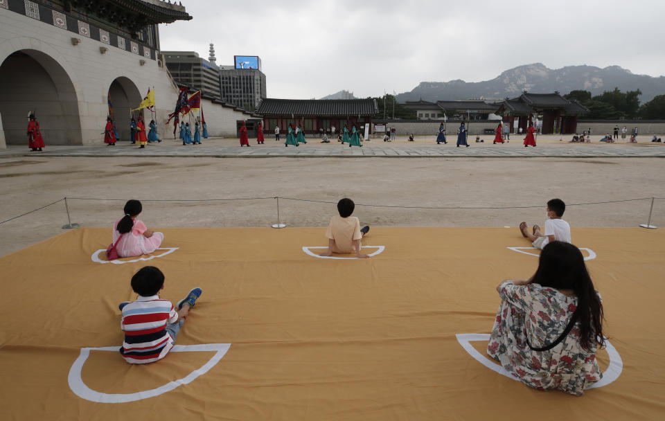 Visitors watch while maintaining social distancing during a re-enactment ceremony of the changing of the Royal Guard at the Gyeongbok Palace, one of South Korea's well-known landmarks, in Seoul, South Korea, Friday, July 31, 2020. South Korea's newest coronavirus cases were mostly tied to international arrivals. (AP Photo/Lee Jin-man)