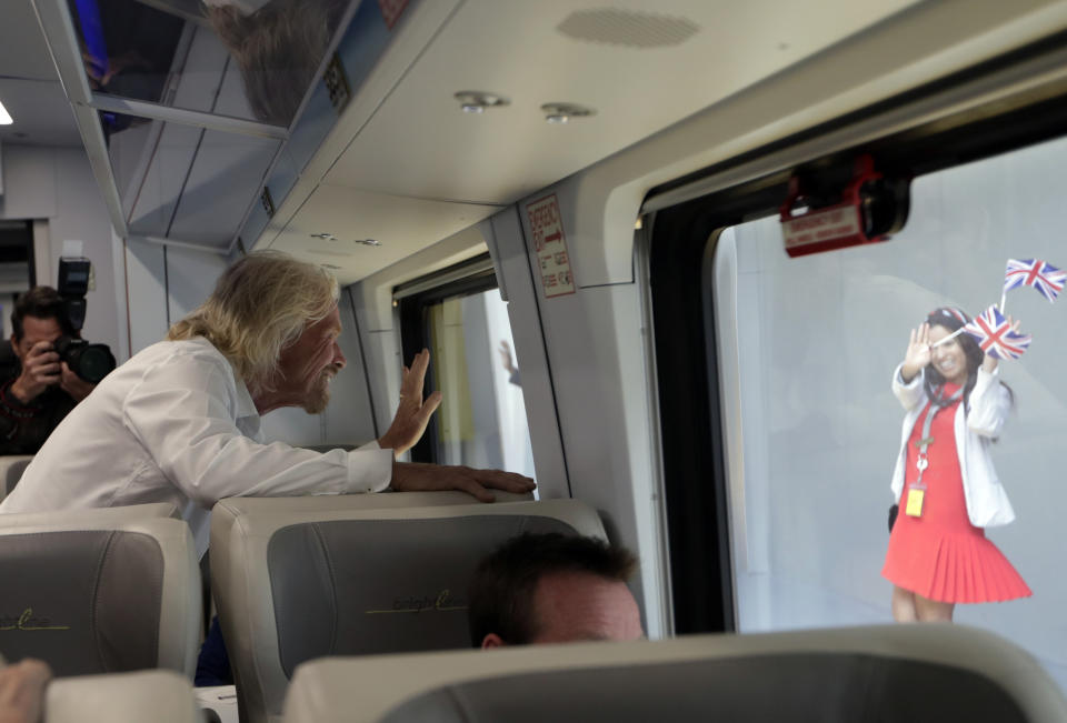 An employee holding British flags waves as Richard Branson, of Virgin Group, left, departs on a Brightline train bound for Miami, Thursday, April 4, 2019, in West Palm Beach, Fla. The state's Brightline passenger trains are being renamed Virgin Trains USA after Branson invested in the new fast-rail project that is scheduled to connect Miami with Orlando. (AP Photo/Lynne Sladky)