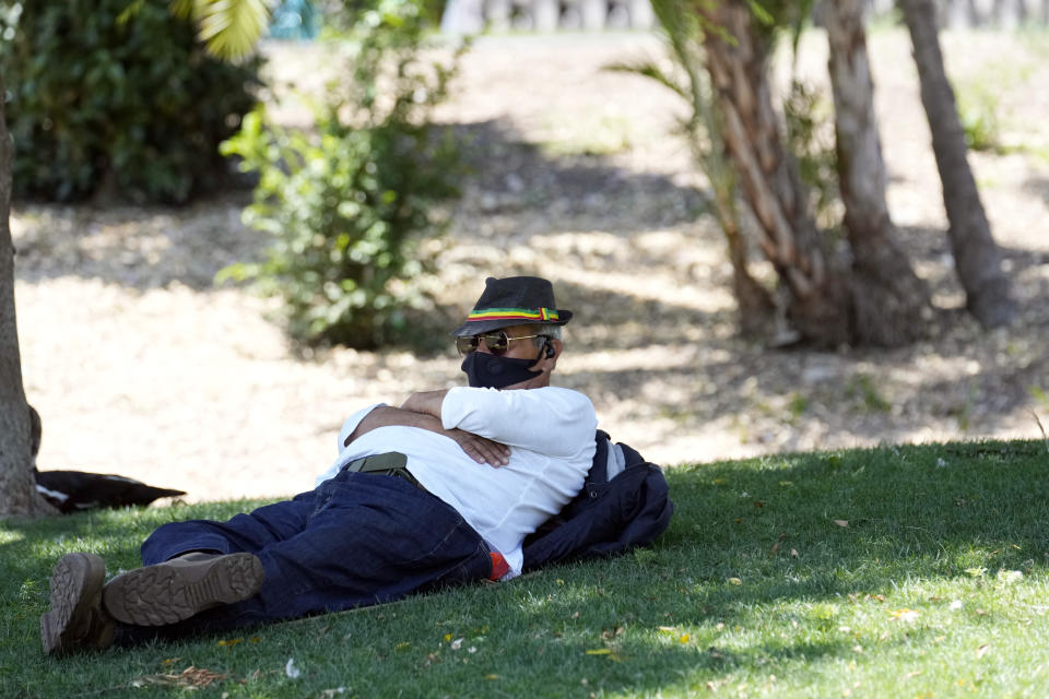 A man sits under the shade of a tree as temperatures rise at MacArthur Park, Tuesday, July 11, 2023, in Los Angeles. (AP Photo/Marcio Jose Sanchez)