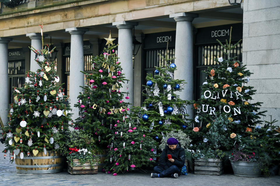 A woman sits amid Christmas trees in Covent Garden, in London, Tuesday, Nov. 24, 2020. Haircuts, shopping trips and visits to the pub will be back on the agenda for millions of people when a four-week lockdown in England comes to an end next week, British Prime Minister Boris Johnson said Monday. (AP Photo/Alberto Pezzali)