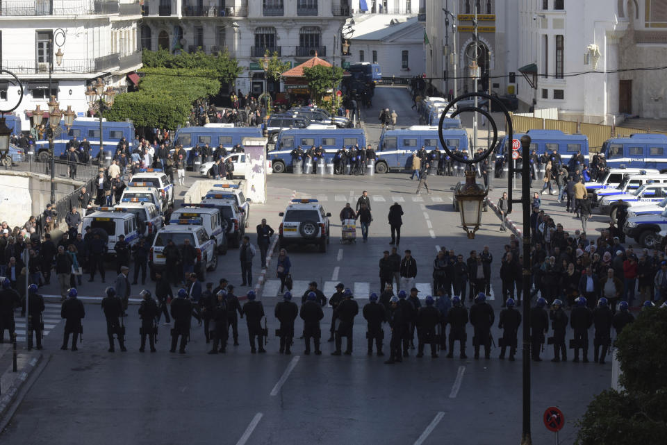 Security forces stand guard as Algerian demonstrators take to the streets in the capital Algiers to protest against the government and reject the upcoming presidential elections, in Algeria, Wednesday, Dec. 11, 2019. Algeria's powerful army chief promises that a presidential election on Thursday will define the contours of a new era for a nation where the highest office has stood vacant for eight months. The tenacious pro-democracy movement which forced leader Abdelaziz Bouteflika to resign after 20 years in power doesn't trust the confident claim and is boycotting the vote. (AP Photo/Toufik Doudou)