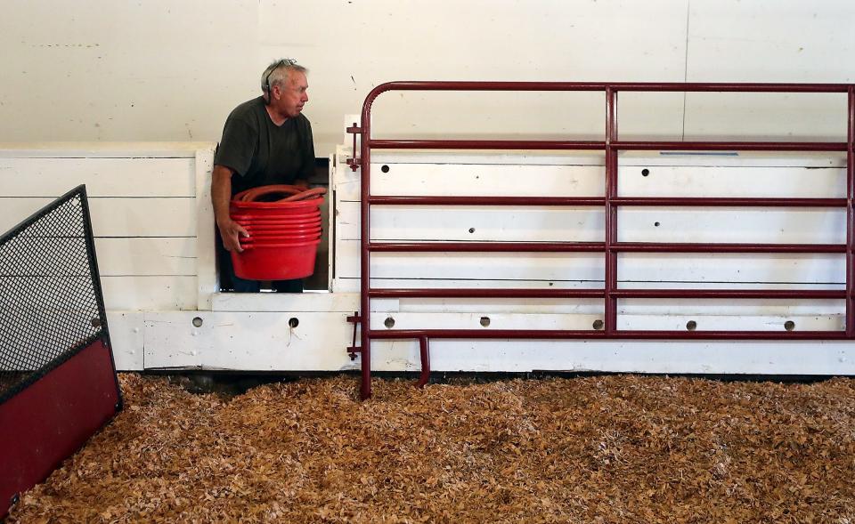 Carl Potts moves a stack of feeding tubs to an area behind the stalls as he helps get the Beef Barn ready for the Kitsap County Fair and Stampede on Monday.