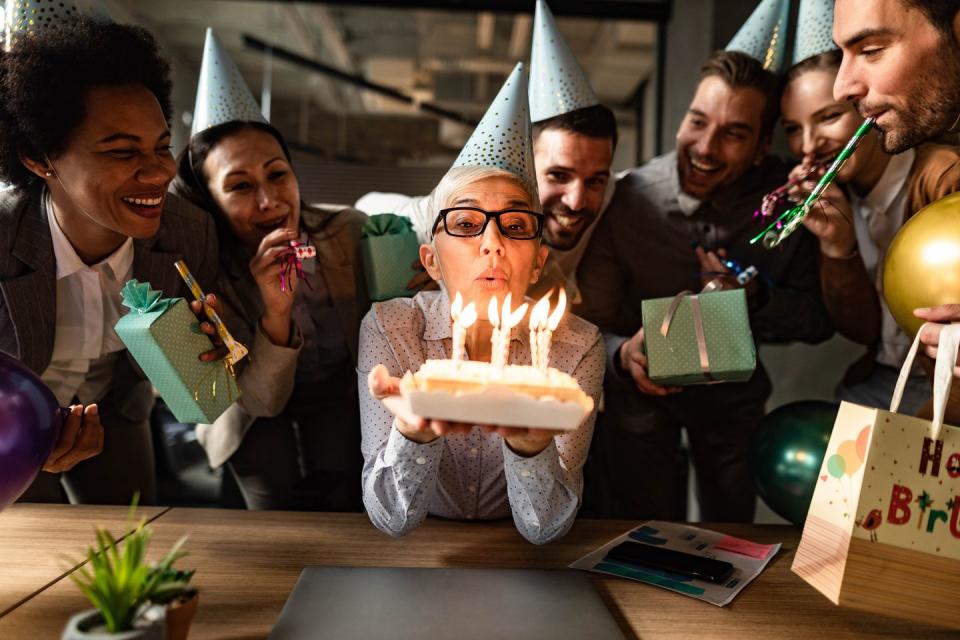 senior businesswoman blowing birthday candles from a cake while having a party with her colleagues