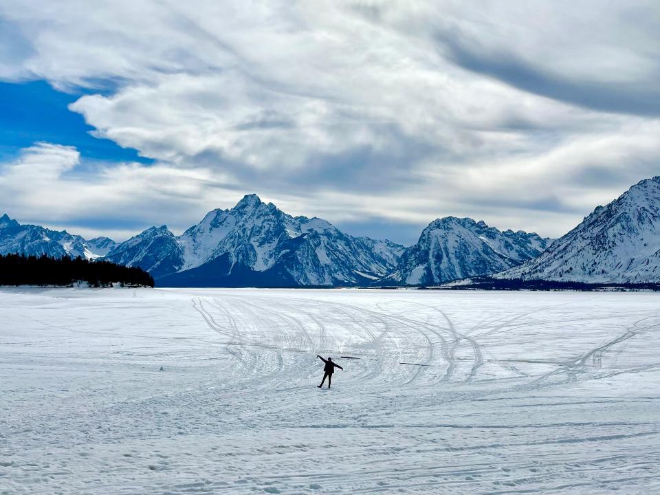 A person standing in a vast, snow-covered Wyoming field surrounded by huge mountains