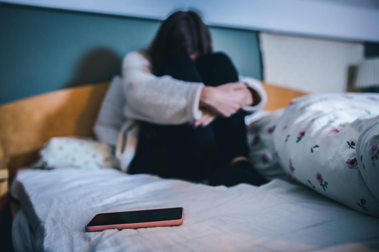 Sad teen with a phone in her bedroom