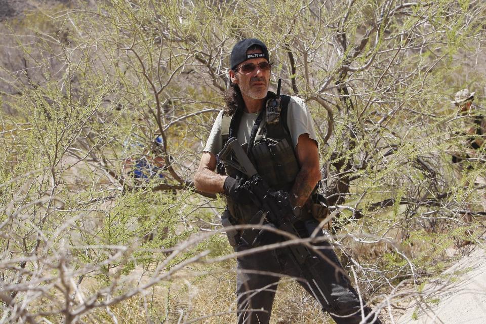 An armed civilian waits nearby in some bushes as the Bundy family and their supporters gather together under the I-15 highway just outside of Bunkerville, Nev. in order to confront the Bureau of Land Management and demand the release of their impounded cattle on April 12, 2014. (AP Photo/Las Vegas Review-Journal, Jason Bean)